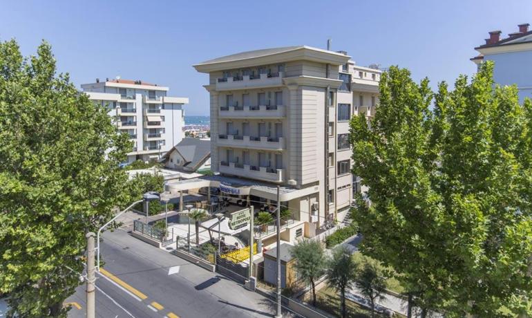 Hotel elegante tra alberi verdi, cielo azzurro e strade animate.