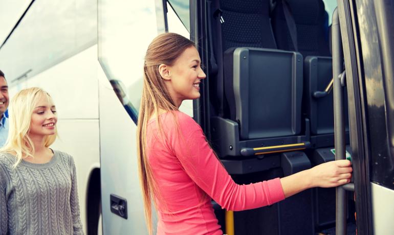 Tre persone sorridenti salgono su un autobus, atmosfera di gioia e avventura.